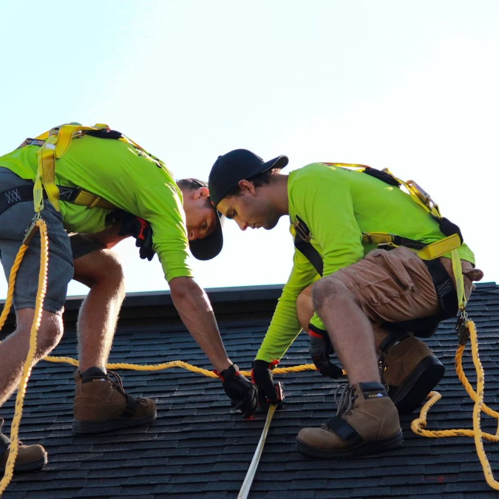 Roofing contractors installing shingles with safety equipment in Chambers County, TX