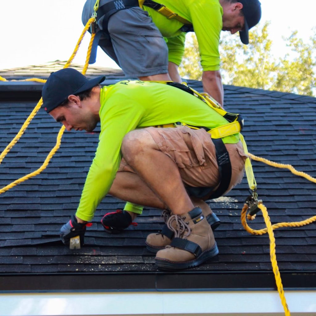 Roofing contractors installing asphalt shingles with safety equipment for roofing services near me