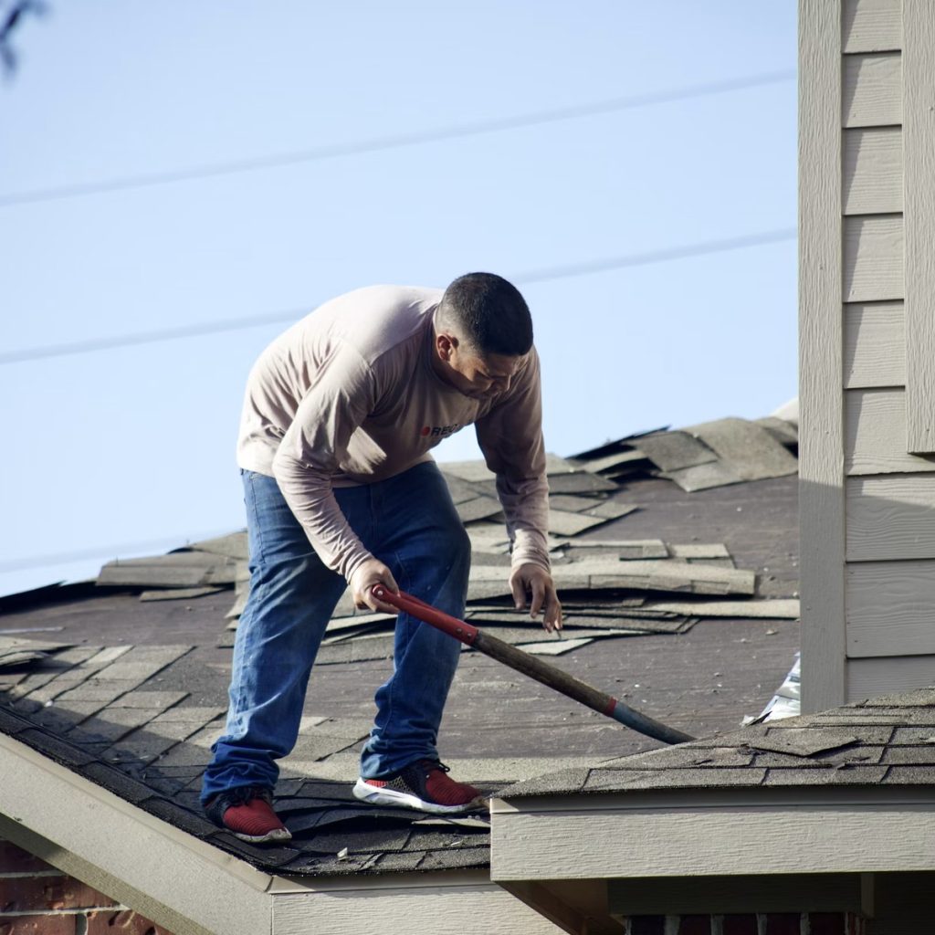 Roofing contractor removing damaged shingles from a residential roof for roofing services near me